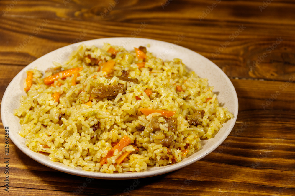 Pilaf with meat, rice, carrot and onion in a plate on wooden table