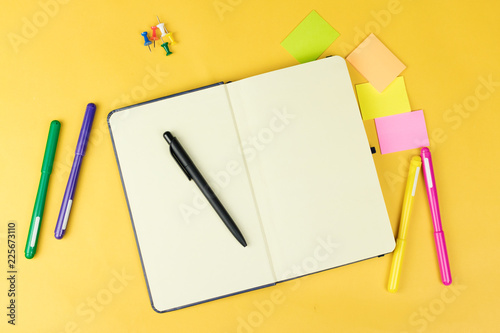 Top view of blank notebook and school supplies like colored markers, sticker and clipers on yellow background. . photo