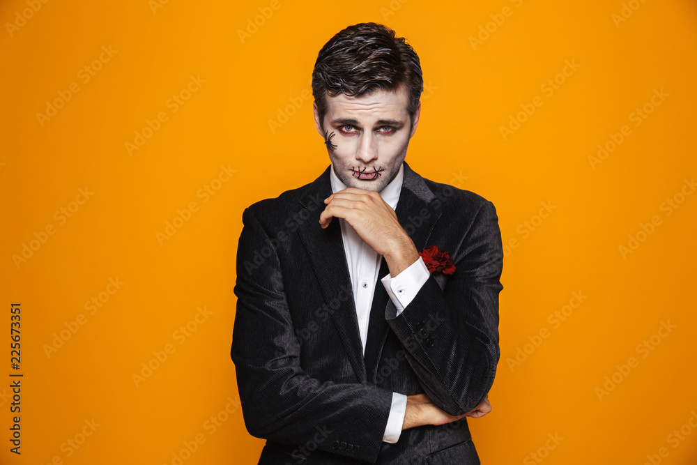 Photo of scary zombie fiance on halloween wearing classical suit and creepy makeup looking at camera, isolated over yellow background Photo of scary zombie fiance on halloween wearing classical suit and creepy makeup looking at camera, isolated over yellow background