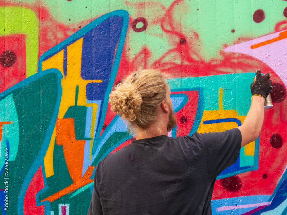 Naklejka premium young man use his talent and feeling for art to apply this with various colors to a city wall
