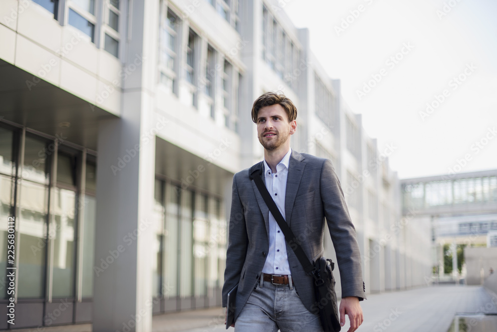 Smiling businessman with crossbody bag in the city on the move Smiling businessman with crossbody bag in the city on the move