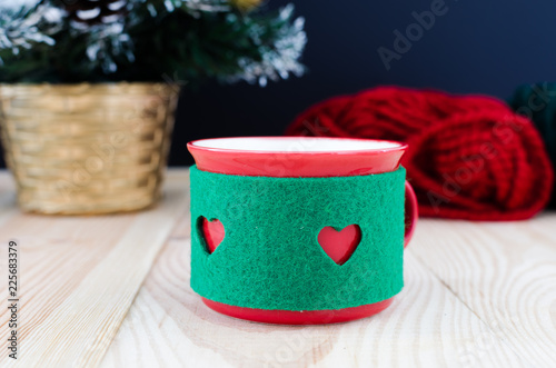 A cup of coffee is standing in front of a christmas tree and skeins of yarn on the wooden table on a black background photo