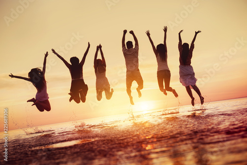 Group of happy friends jumps in sunset water