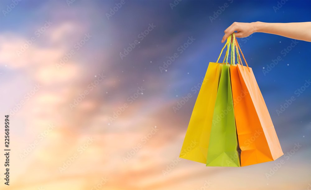 sale, consumerism and concept - close up of male hand holding shopping bags over sky background