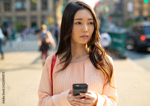 Asian woman in city walking using cell phone