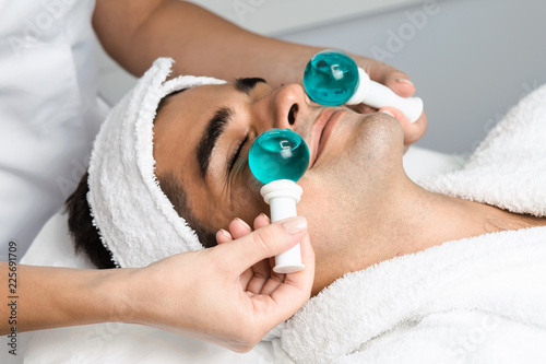 Young good looking man in beauty salon during treatment with a cold glass balls. Cryo therapy. Face and skin care. photo