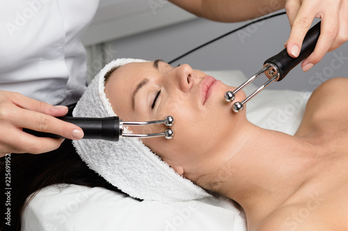 Beautiful woman receiving facial microcurrent treatment at spa salon. Beautician using electrical impulses for facial procedures. photo