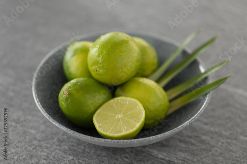 food, healthy eating and vegetarian concept - close up of limes in bowl on slate table top