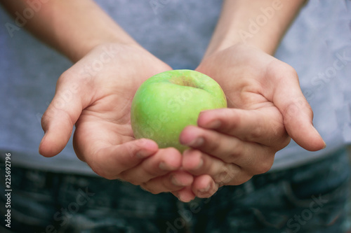hands of a girl holding a green apple offering it to us, close-up, open air