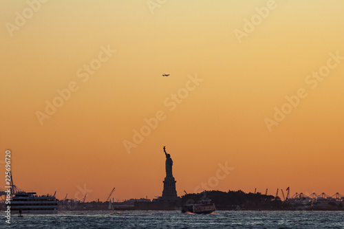 Lady Liberty with a orange sky background. Ships in the water and a plane flying over