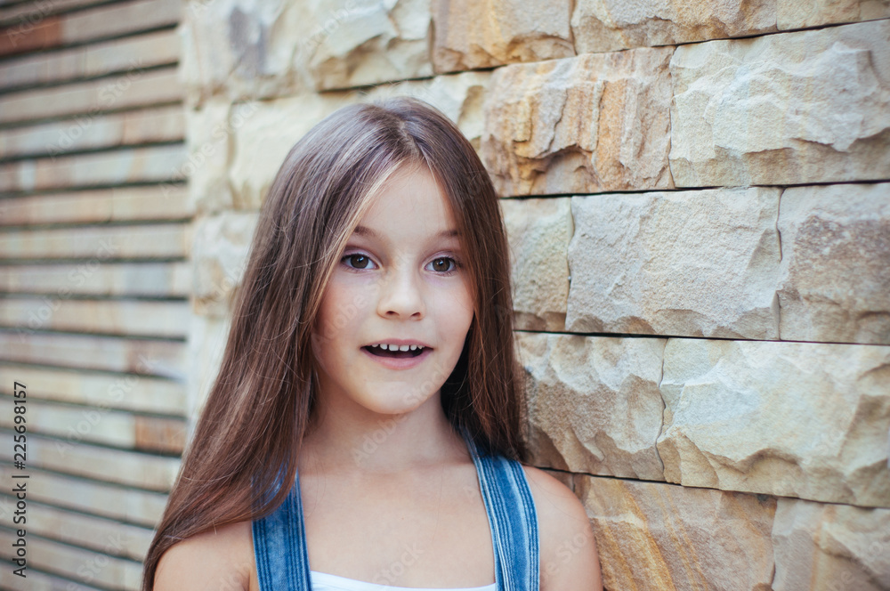 Model little beautiful girl with long hair, street fashion near the wall on a summer Model little beautiful girl with long hair, street fashion near the wall on a summer