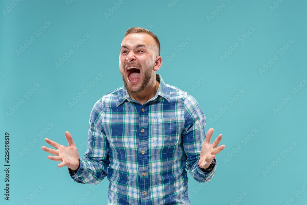 Fototapeta premium Screaming, hate, rage. Crying emotional angry man screaming on blue studio background. Emotional, young face. male half-length portrait. Human emotions, facial expression concept. Trendy colors