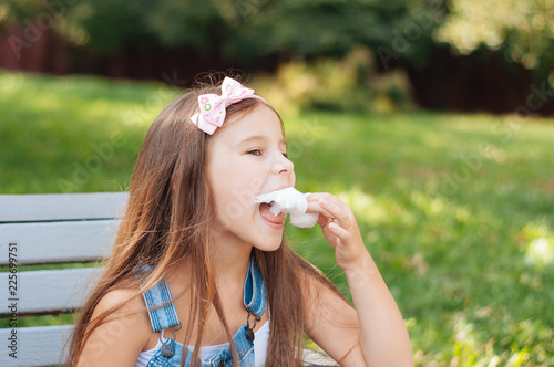 little girl eating cotton candy sitting on a bench in the park summer