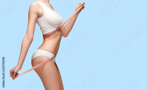 The girl taking measurements of her body, blue studio background.