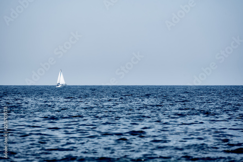 A view of the sea, a white yacht with sails and the sky.