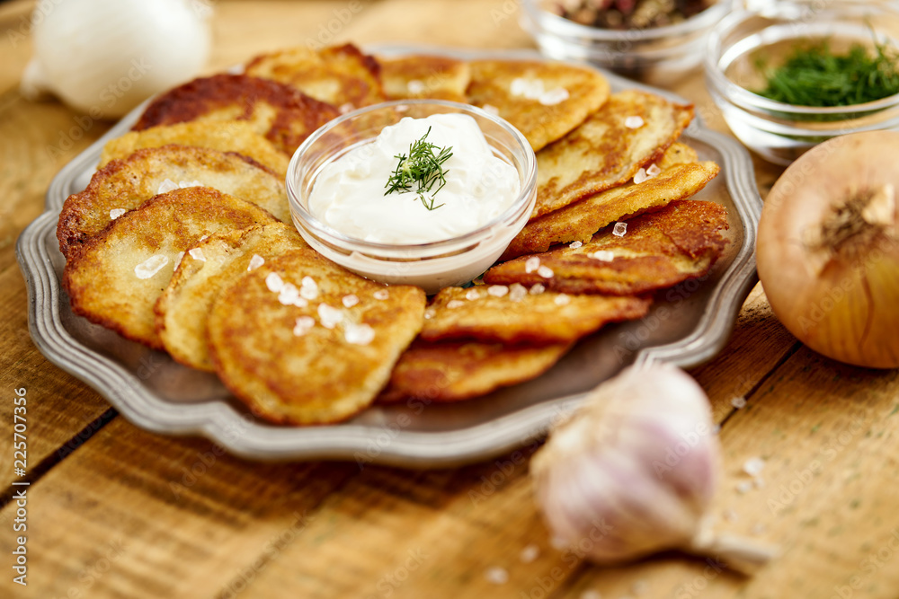 metal plate with delicious potato pancakes on an old wooden table with garlic onions and toppings in the kitchen metal plate with delicious potato pancakes on an old wooden table with garlic onions and toppings in the kitchen