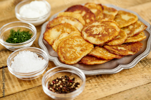 metal plate with delicious potato pancakes on an old wooden table with bowls full of additions in the kitchen