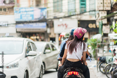Women in colorful helmets riding a bicycle down the streets of Hanoi, Vietnam. Street traffic and shops in the capital city.