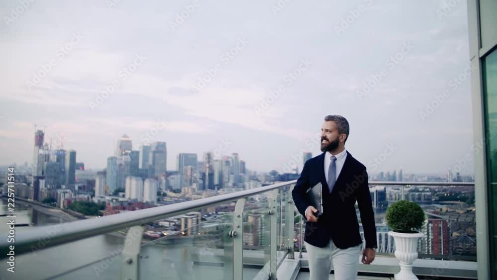 A portrait of businessman walking on a terrace against London view panorama. A portrait of businessman walking on a terrace against London view panorama.