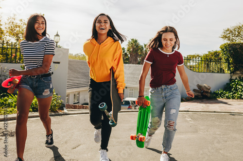 Schilderij op canvas Teenage girls walking on street holding skateboards