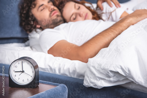 Fotografie close-up view of alarm clock and young couple sleeping together behind