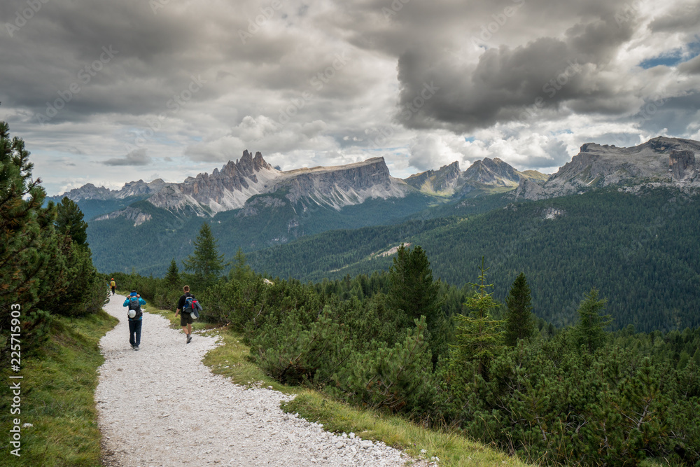 climbers walking down a road in a Dolomite mountain landscape after a hard climb with a great panorama view behind them of the Alta Badia mountains