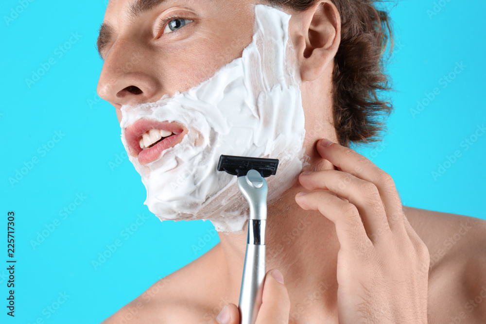 Handsome young man shaving on color background