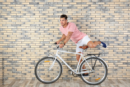 Handsome young hipster man riding bicycle near brick wall