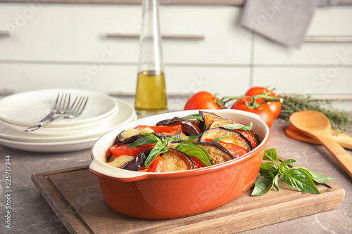 Baked eggplant with tomatoes, cheese and basil in dishware on table