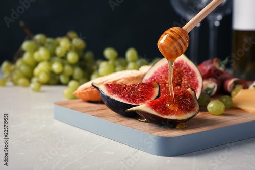Konstfotografi Pouring honey onto ripe fig slices on wooden board, closeup