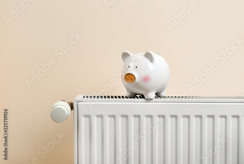 Piggy bank on heating radiator against light background
