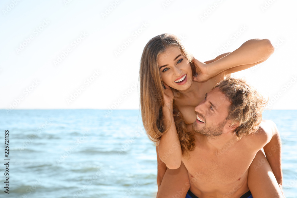 Happy young couple in beachwear having fun together on seashore. Space for text