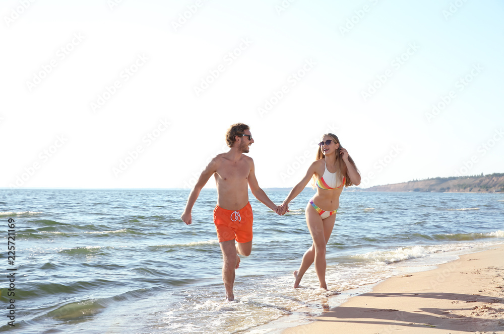Happy young couple in beachwear running together on seashore