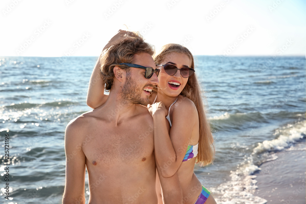 Happy young couple in beachwear spending time together on seashore