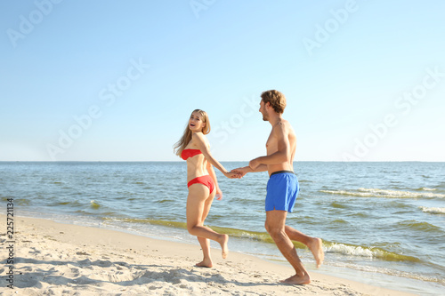 Happy young couple in beachwear running together on seashore © New Africa