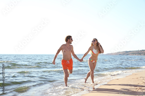 Happy young couple in beachwear running together on seashore