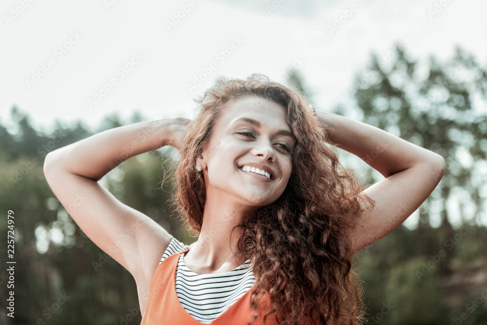 Broad smile. Appealing good-looking beaming curly dark-haired woman smiling broadly while having rest in natural environment