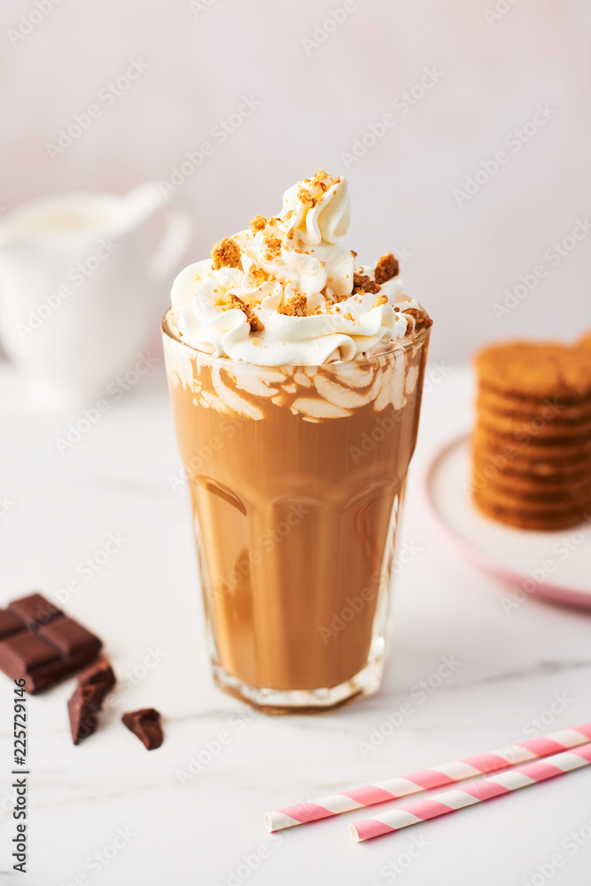 Chocolate ice coffee with whipped cream and cookies in a tall glass with pink straws on white marble table over rose background. High resolution image with copy space and selective focus.