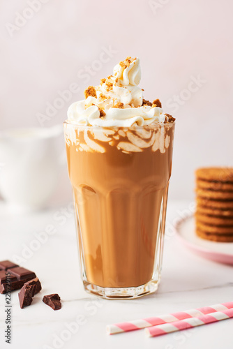 Chocolate ice coffee with whipped cream and cookies in a tall glass with pink straws on white marble table over rose background. High resolution image with copy space and selective focus.