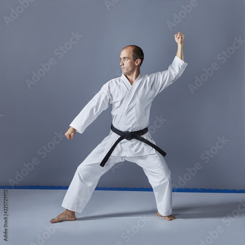 On a gray background an athlete in white karategi is doing formal karate exercises.