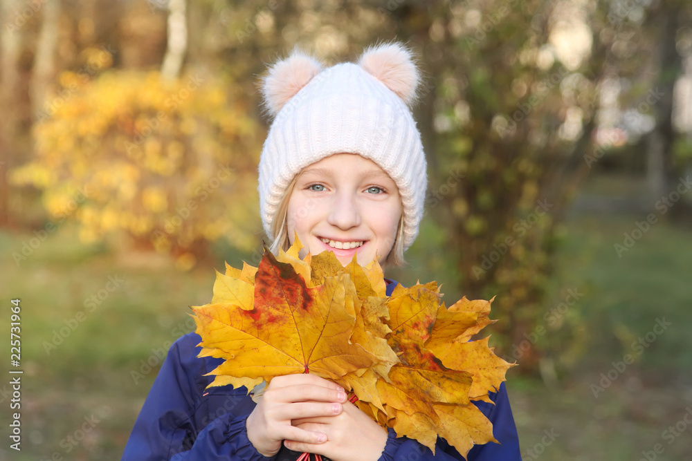 Happy smiling kid girl in a warm knitted hat collects bouquet of yellow leaves. Autumn, walk in the park. Happy smiling kid girl in a warm knitted hat collects bouquet of yellow leaves. Autumn, walk in the park.