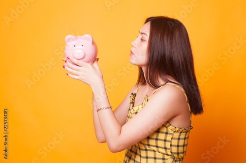 Young Asian woman kiss a pink coin bank.