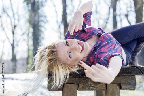 Blonde girl laying on table in nature with middle fingers up on hand