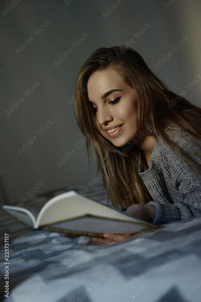 Young woman reading book lying in bed. Teenage girl enjoying a book in cozy bedroom. Natural low light, no retouch, matte grainy filter. Young woman reading book lying in bed. Teenage girl enjoying a book in cozy bedroom. Natural low light, no retouch, matte grainy filter.