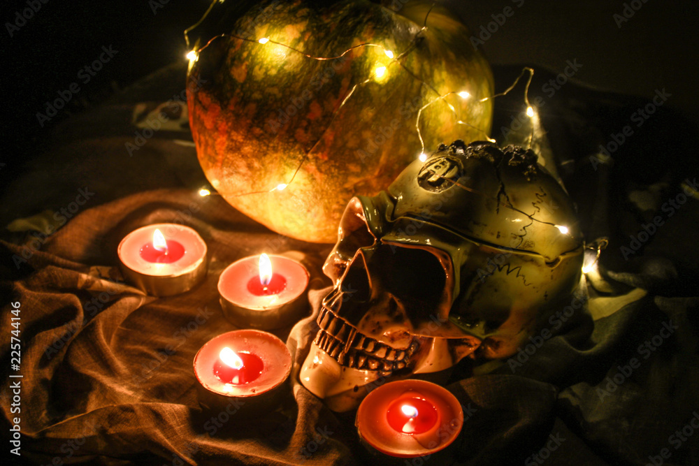 Helloween skull and pumpkin  in the dark with a garland.Warm light and brown candles