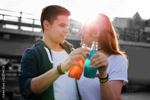 Drinking together. Cheerful young people relaxing and smiling while hugging and holding bottles with colorful lemonade