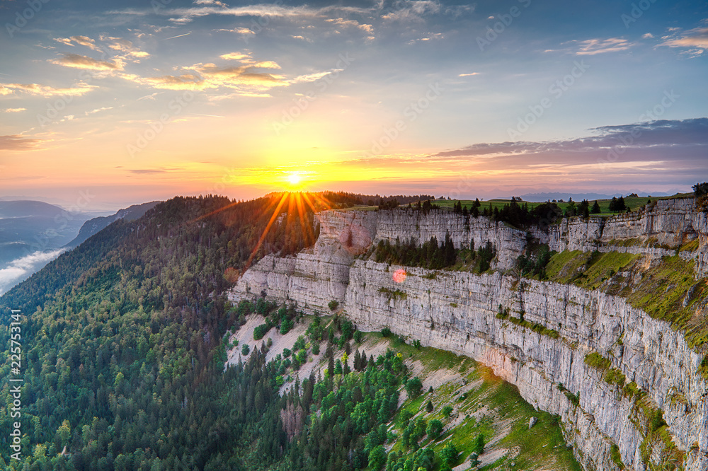 Vivid sunset with sunstar over cliff Creux du Van Neuchatel in warm light with sceenic view on valley and green forest - obrazy, fototapety, plakaty 