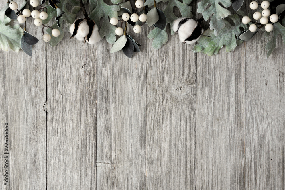 Top border of silver green leaves and white berries over a rustic gray wood background. Top view with copy space.
