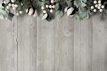 Top border of silver green leaves and white berries over a rustic gray wood background. Top view with copy space.