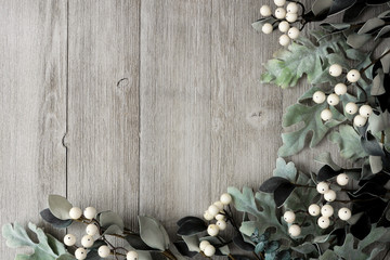 Corner border of silver green leaves and white berries over a rustic gray wood background. Top view with copy space.